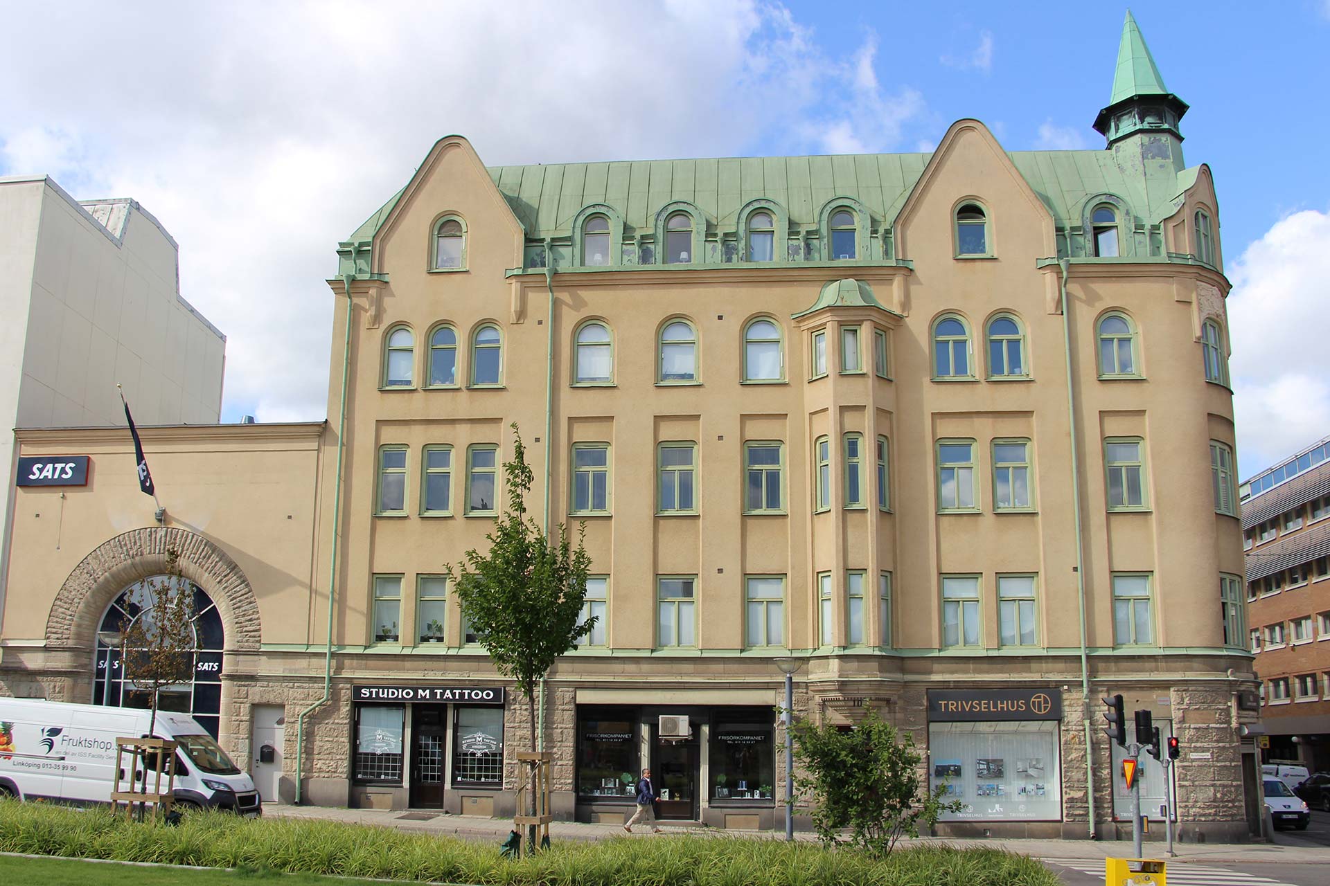 A big yellow-brown building with a green roof against a blue sky.