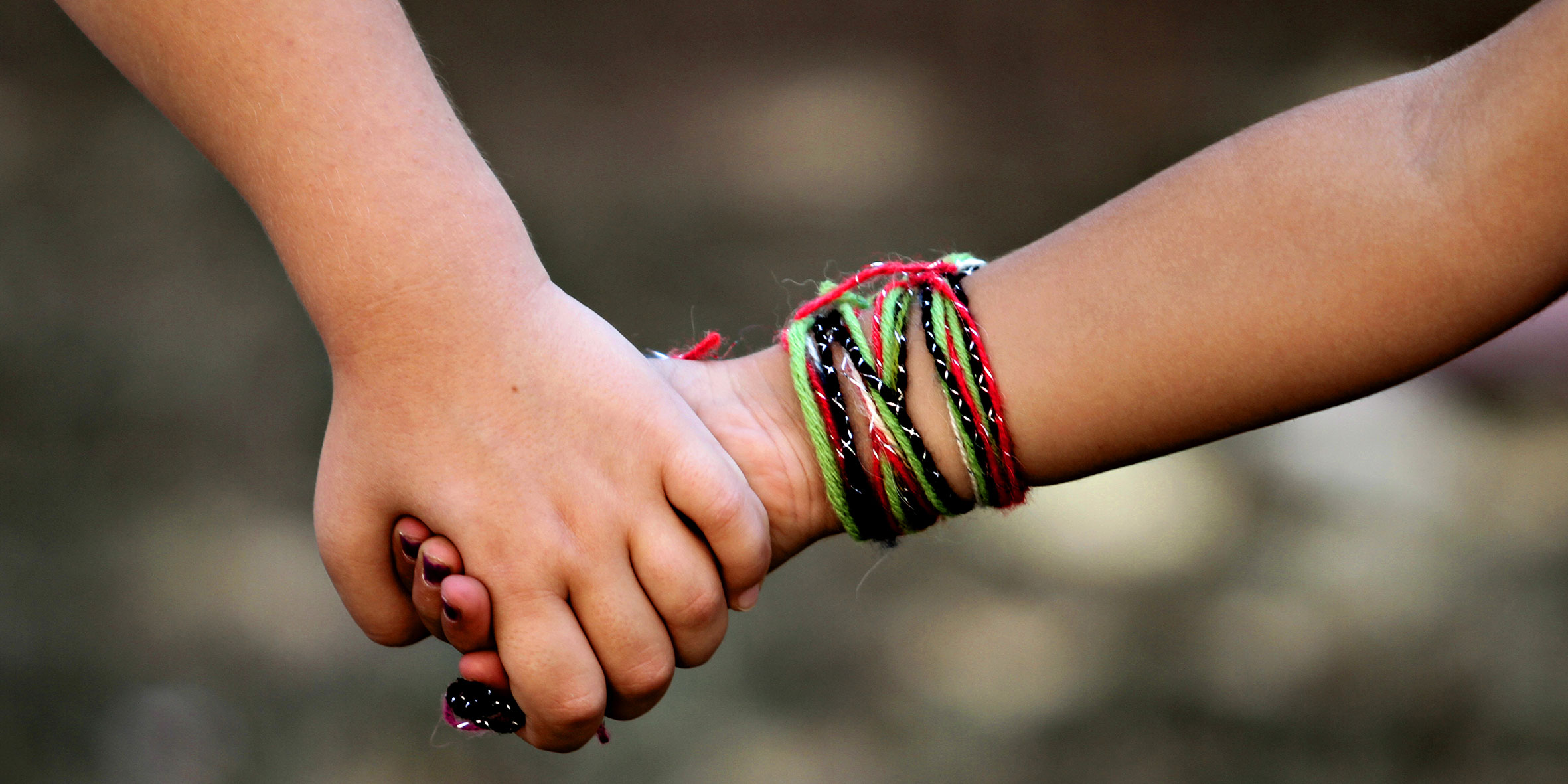 Two people holding hands, one can only see the hands. One of the people has colourful braces.