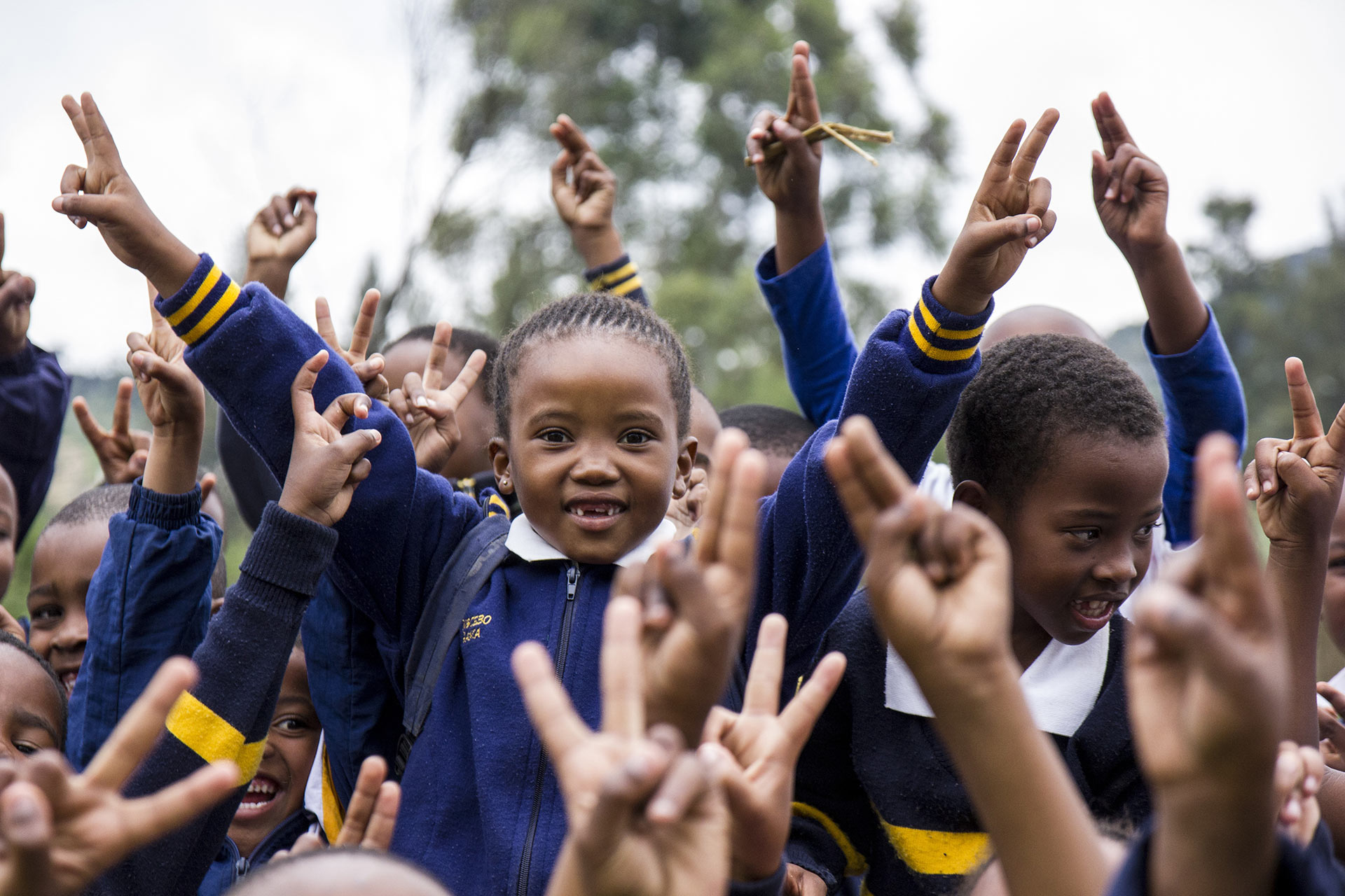 Many children in school uniforms laughing with their hands in the air