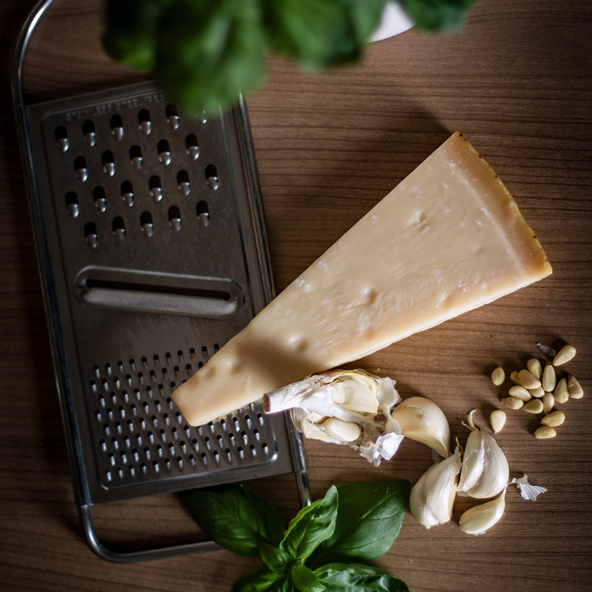 A grater on a cutting board along with a piece of cheese, basil and garlic