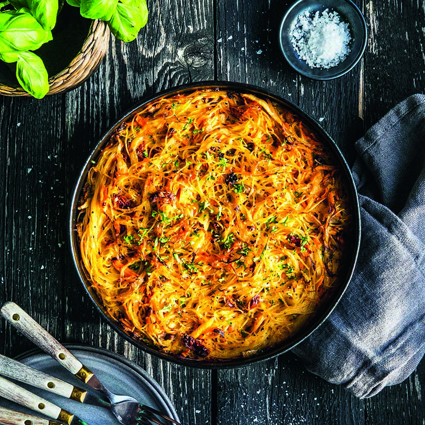 A black plate of spaghetti au gratin with butter-fried cabbage on a black wooden table