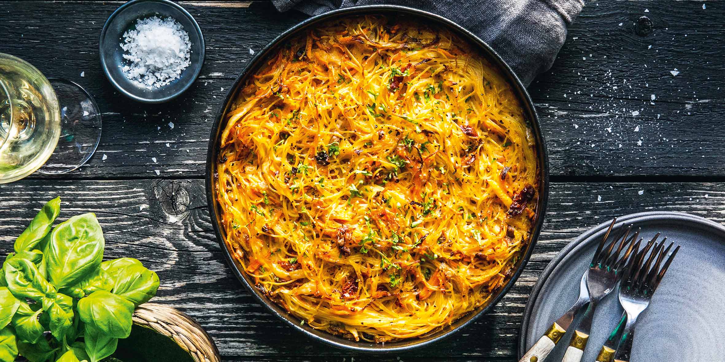 A black dish of spaghetti au gratin with butter-fried cabbage on a black wooden table