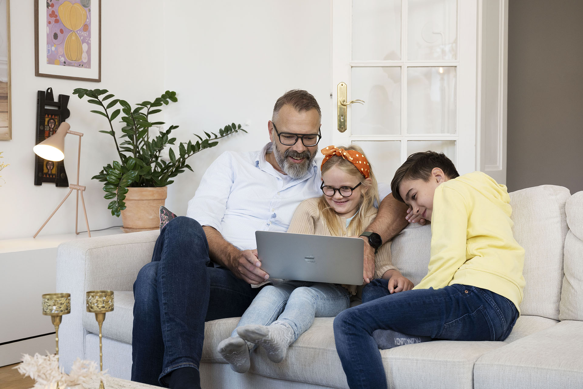A man and two children are sitting on a white sofa and laughing at something on the computer