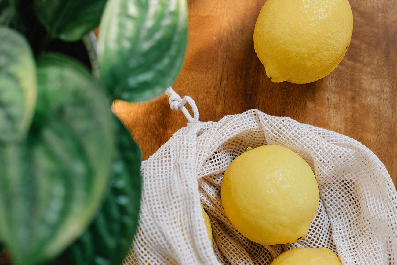 A kitchen wooden bench with three lemons on it, two of which are in a white net bag.