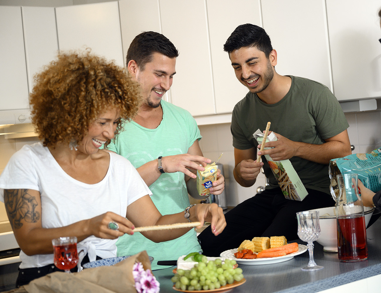 A girl with curly hair and two boys with dark hair and short-sleeved shirts are standing in a kitchen preparing a fruit platter.