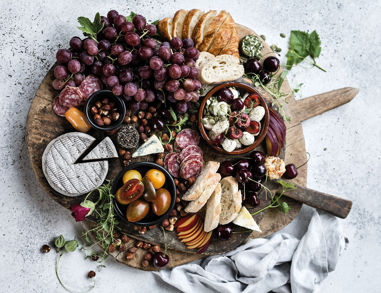 A wooden cutting board with cheeses, sausages, biscuits, grapes and figs.
