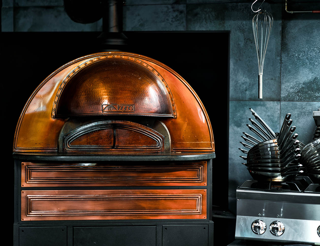 A pizza oven with brass details in a grey-tiled kitchen.