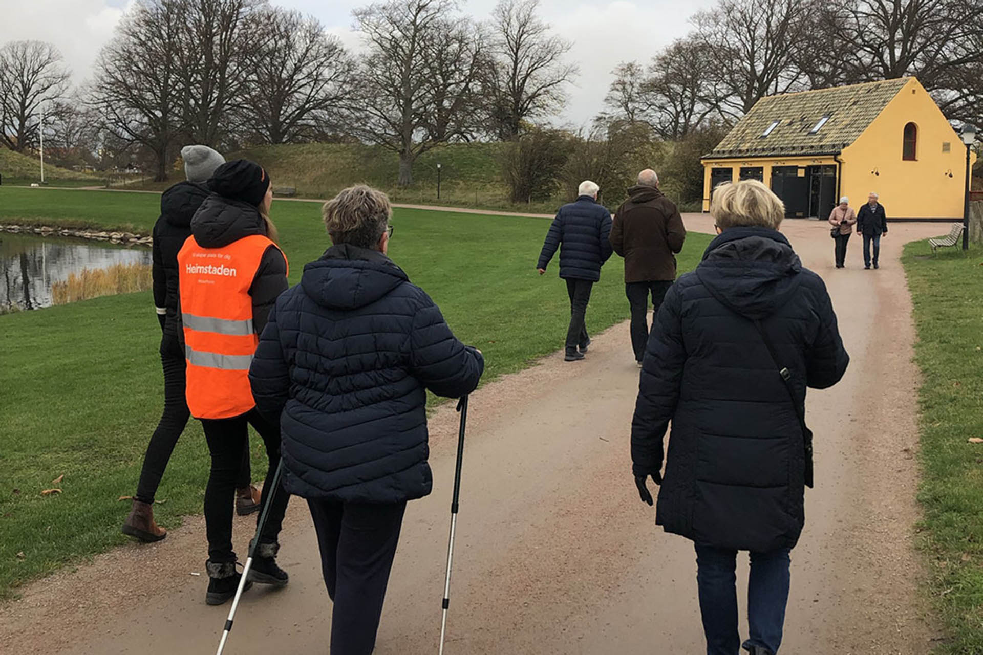 People out walking on a gravel road with a yellow house in the background.