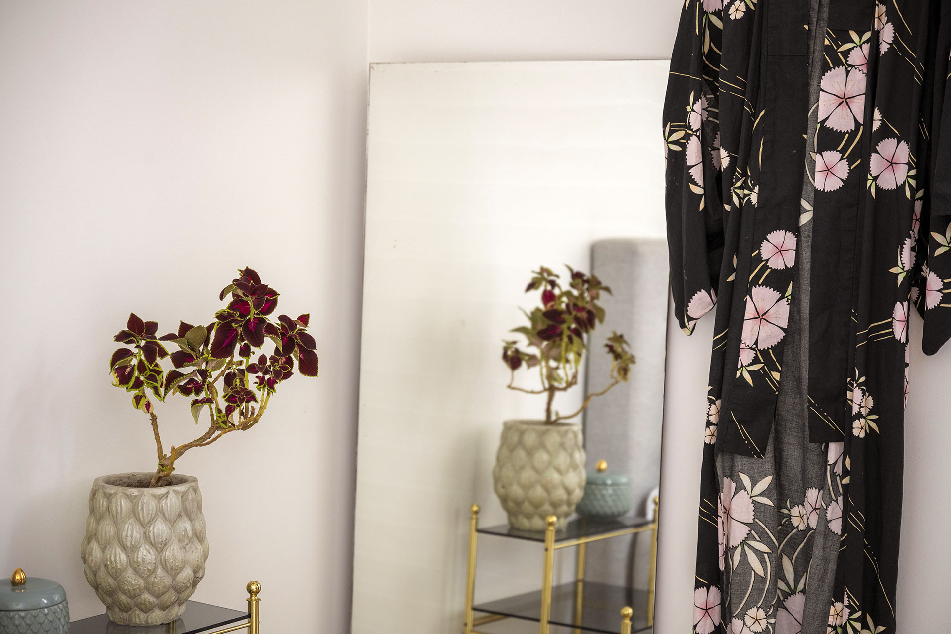 A room with pink walls has a mirror and a bathrobe with flowers on it. A vase on a table is reflected in the mirror.