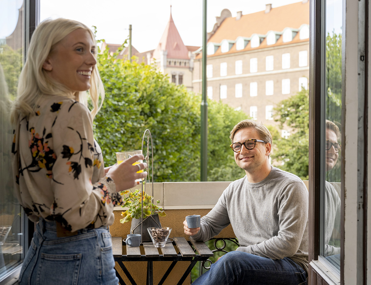A person is sitting on a balcony looking at a person who is standing next to a table.