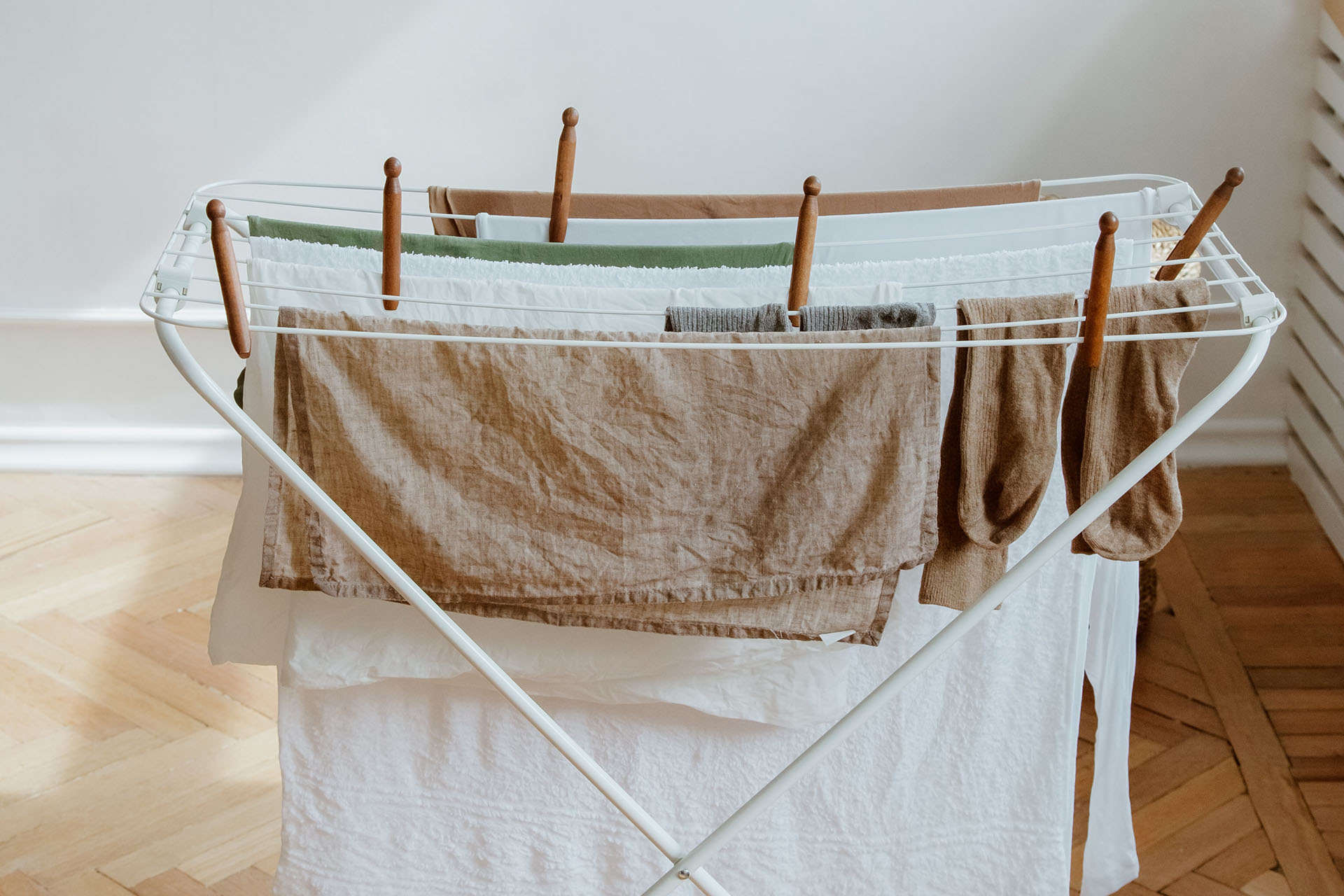 A white drying rack with light towels and white sheets and clothespins made of wood