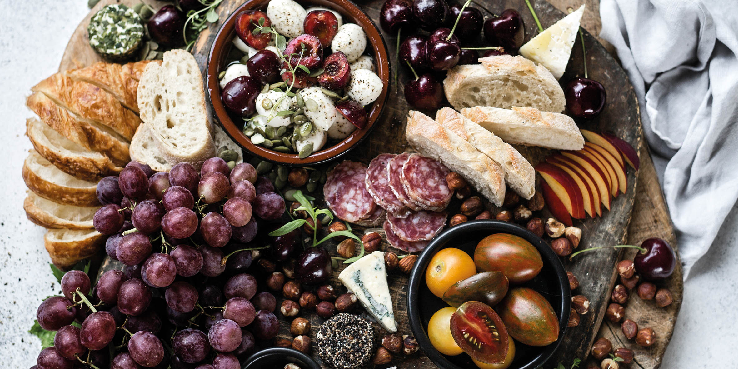 A wooden platter with cheese, crackers, grapes and other tasty foods.