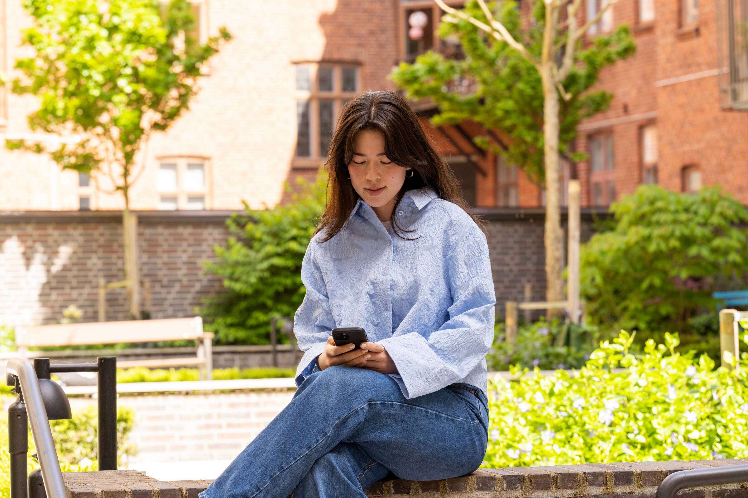 Kvinne sitter utendørs og ser på en mobiltelefon