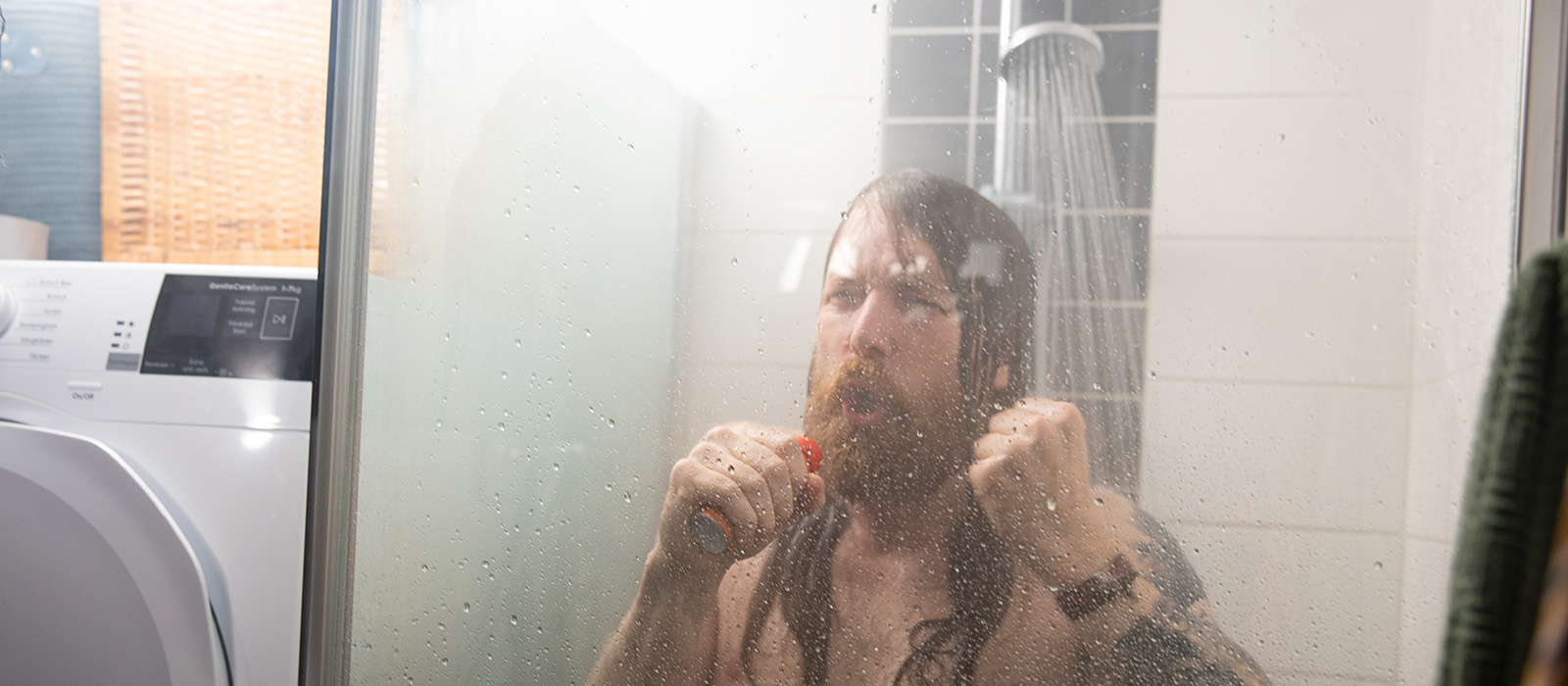 En man med långt hår står i duschen och sjunger