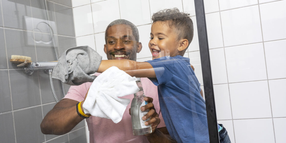 En man i rosa tshirt och en pojke i blå thirt står i en dusch och rengör glaset