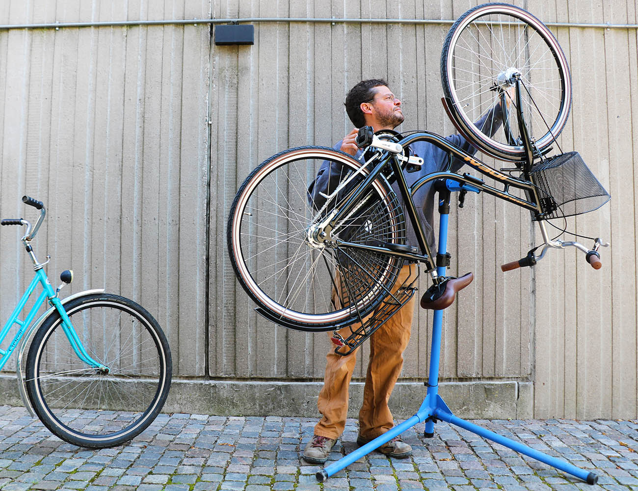 En kille med blå tröja och bruna byxor står vid en cykel som hänger upp och ner på gatan
