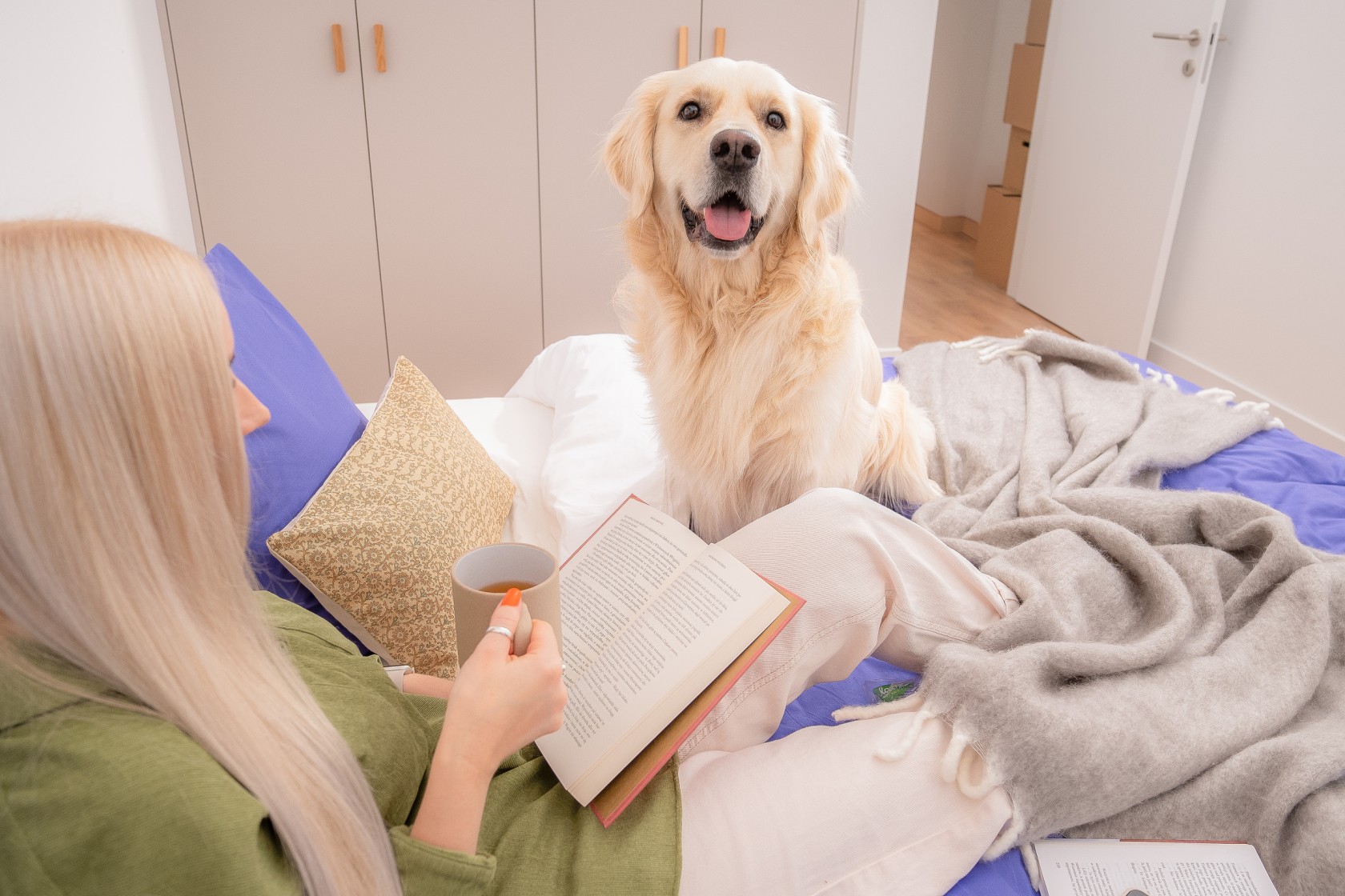 Haustierbesitzer liest im Bett, Hund schaut in die Kamera